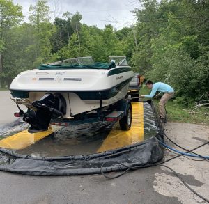 A boat pulled into the washing station and being sprayed with a host by a young man.